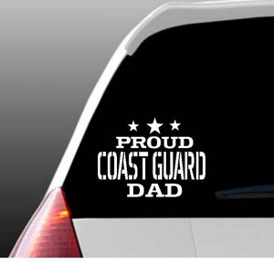May include: White vinyl decal with the text "Proud Coast Guard Dad" and three stars above the text. The decal is on the back window of a car.