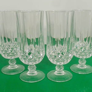 May include: Four clear crystal champagne flutes. Each glass features a diamond-cut pattern on the lower half and vertical lines on the upper half. The glasses have a round base and a decorative stem.
