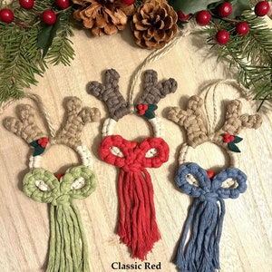 May include: Three handmade macrame reindeer ornaments with different colored tassels. The reindeer are made with natural twine and have a brown felt nose. The tassels are apple green, classic red, and denim blue.