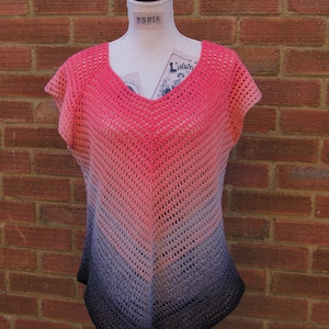 Puede incluir: Un top de crochet con cuello en V y mangas cortas. El top está hecho con un hilo degradado que pasa del rosa al morado al negro. El top se muestra en un maniquí contra una pared de ladrillo.