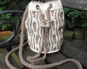 Puede incluir: Un bolso de cubo de crochet con un patrón de rayas marrones y blancas. El bolso tiene una correa larga marrón y un cierre de cordón.