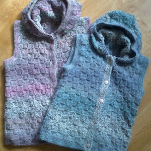 May include: Two knitted hooded vests, one in a pink and grey ombre pattern and the other in a blue and grey ombre pattern.