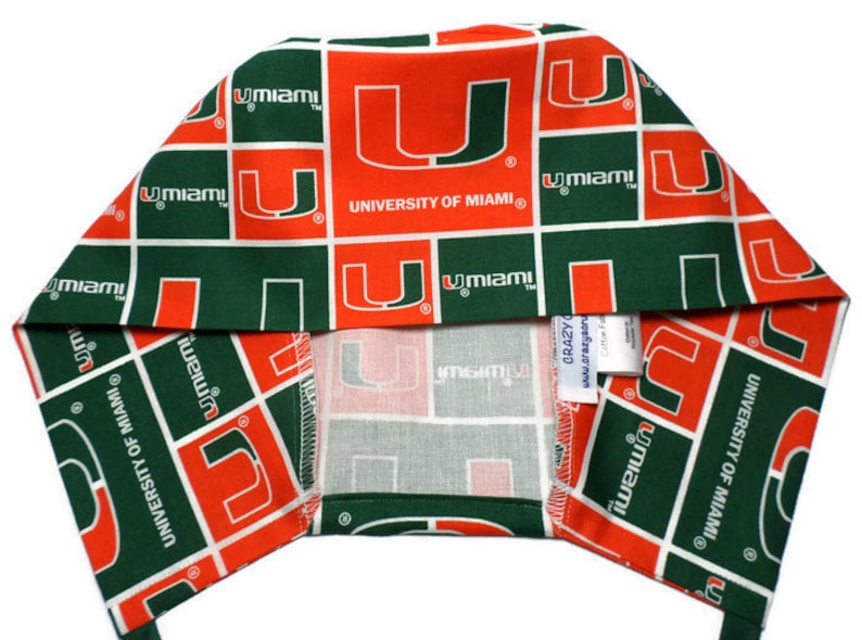 Puede incluir: Un turbante de tela verde y naranja con el logotipo de la Universidad de Miami repetido en toda la superficie. El logotipo es una 'U' blanca dentro de un cuadrado naranja con las palabras 'University of Miami' en texto blanco.