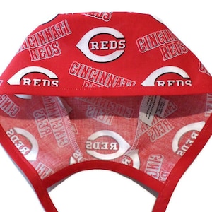 May include: Red and white baseball cap with the Cincinnati Reds logo and text repeated on the fabric. The cap has a tie at the back.