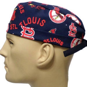 May include: A blue and red surgical scrub hat with a St. Louis Cardinals baseball team theme. The hat features the team's logo, mascot, and the words "St. Louis Cardinals".