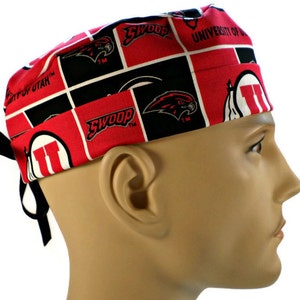 May include: A red, black, and white patterned surgical scrub cap featuring the University of Utah logo and the word "SWOOP". The cap is made of fabric and has black ties.