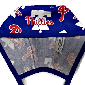 May include: Blue and white patterned surgical cap with the words "Phillies" and a Liberty Bell graphic. The cap has a blue trim.