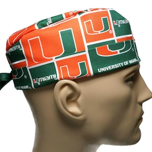 Puede incluir: Un gorro de quir&oacute;fano verde y naranja con el logotipo de la Universidad de Miami repetido en toda la tela. El gorro tiene un lazo en la parte posterior.