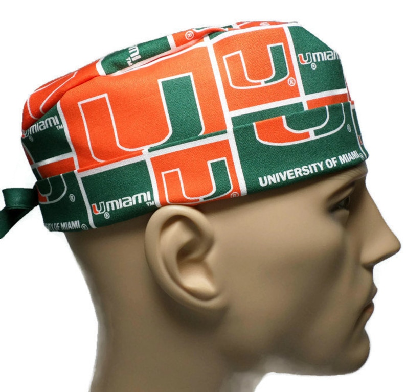 Puede incluir: Un gorro de quir&oacute;fano verde y naranja con el logotipo de la Universidad de Miami repetido en toda la tela. El gorro tiene un lazo en la parte posterior.