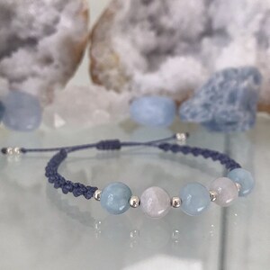 May include: A blue and white beaded bracelet with a gray cord. The bracelet has four beads, two blue and two white.
