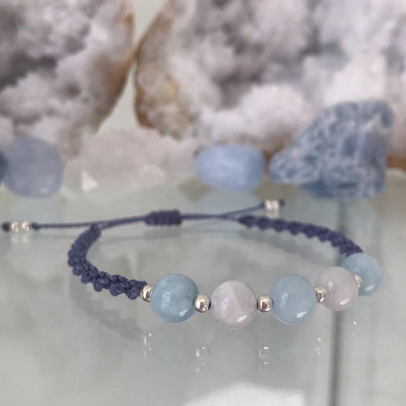 May include: A blue and white beaded bracelet with a gray cord. The bracelet has four beads, two blue and two white.