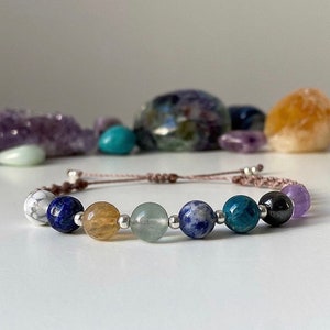 May include: A multi-colored beaded bracelet with a brown cord. The beads are white, blue, yellow, green, blue, green, black, and purple.