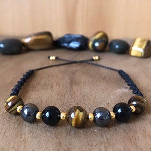 May include: A black cord bracelet featuring tiger's eye, black onyx, and hematite beads. The beads are separated by gold spacers.
