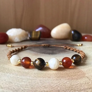 May include: A brown cord bracelet with white, orange, and tiger's eye beads.