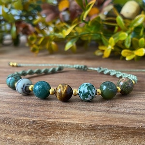 May include: A green and brown beaded bracelet with gold accents. The bracelet is made with a variety of stones, including green agate, tiger's eye, and moss agate.