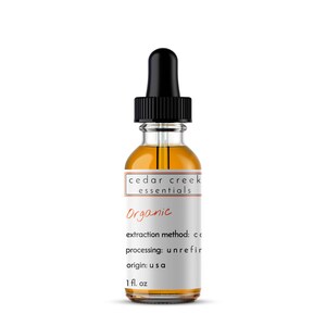 Op de afbeelding: Een doorzichtige glazen fles met een zwarte druppelaar en een wit etiket met de tekst "cedar creek essentials Organic extraction method: co processing: unrefir origin: u s a 1 fl. oz".