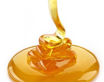 Può includere: Primo piano di miele dorato che cola da un cucchiaio su una superficie bianca.