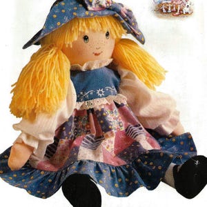 May include: A Holly Hobbie doll pattern by Butterick. The doll has yellow yarn hair, a blue dress with a patchwork skirt, and a matching hat. The pattern number is 146, and the doll is one size.