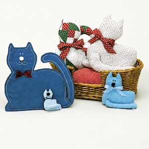 May include: A collection of fabric cat figures including a large blue cat, a small blue cat, and two cats in a wicker basket. The cats feature various patterns and ribbons. Text at the bottom lists materials for Country Cats, including dimensions in inches.