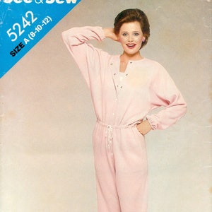 May include: A pink jumpsuit with a drawstring waist and long sleeves. The jumpsuit has a button-up front and a V-neck. The model is wearing white shoes. See & Sew 5242 Size A (8-10-12)