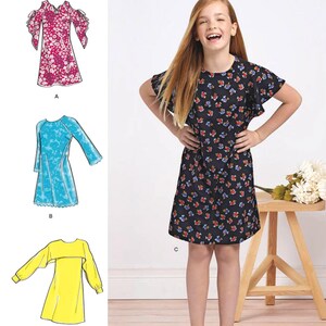 May include: Simplicity sewing pattern 8567 for girls' plus sizes 8-16. The image shows a girl wearing a black floral dress. The pattern includes designs for dresses with various sleeve styles. The Simplicity logo is at the top.
