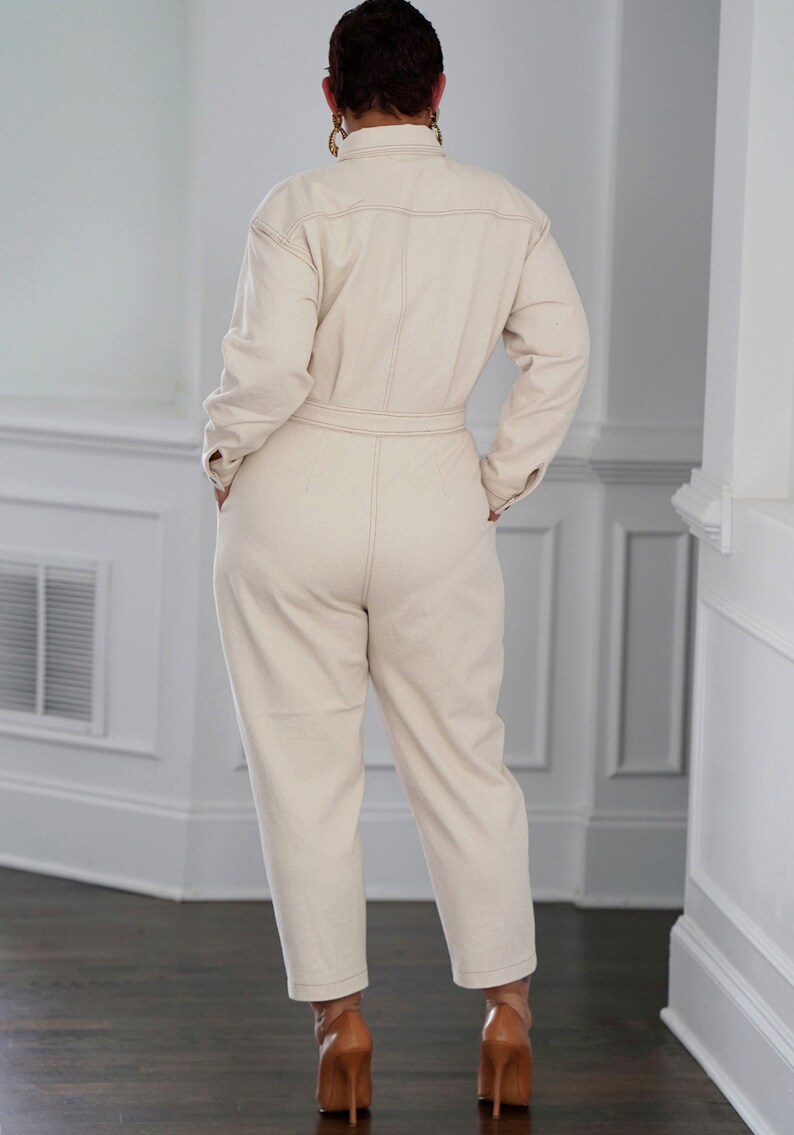 Peut inclure: Une combinaison cr&egrave;me &agrave; manches longues et une ceinture. La combinaison a un col et une fermeture boutonn&eacute;e. Le mannequin porte des talons hauts marrons.