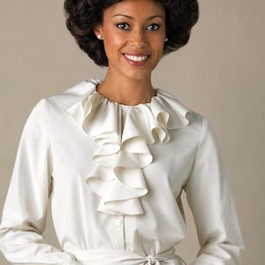 May include: A long-sleeved, off-white blouse featuring a prominent vertical ruffle down the center front, a high neckline, and a matching fabric tie belt at the waist. The garment has a button-down front closure and simple, cuffed sleeves.