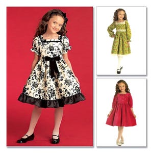 May include: Three girls wearing different styles of dresses. The girl on the left is wearing a white dress with black floral print, a black velvet sash, and a black ruffle trim. The girl in the middle is wearing a green dress with white floral print and white lace trim. The girl on the right is wearing a red dress with white embroidered details.