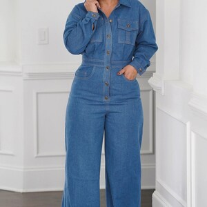 Peut inclure: Une femme portant une combinaison en jean bleu &agrave; manches longues et &agrave; fermeture boutonn&eacute;e. La combinaison a une taille cintr&eacute;e et des jambes larges.