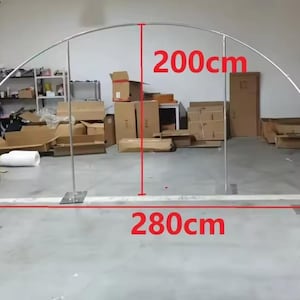 May include: A silver metal archway, 200cm high and 280cm wide, suitable for events. The arch has a curved top and is supported by two vertical posts with square bases. The background shows a cluttered storage area.
