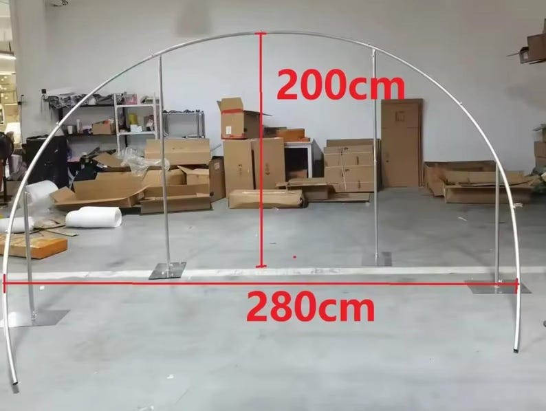 May include: A silver metal archway, 200cm high and 280cm wide, suitable for events. The arch has a curved top and is supported by two vertical posts with square bases. The background shows a cluttered storage area.