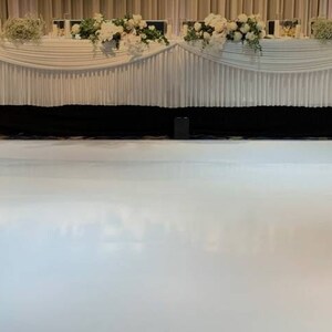 May include: A white dance floor with a white table and white linens in the background. The table is decorated with white flowers.