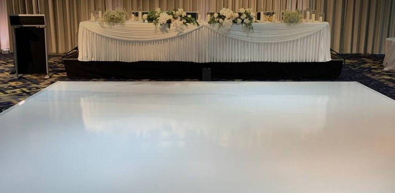 May include: A white dance floor with a white table and white linens in the background. The table is decorated with white flowers.