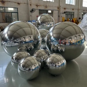 May include: A group of silver inflatable spheres of varying sizes. The spheres are reflective and create a mirrored effect.