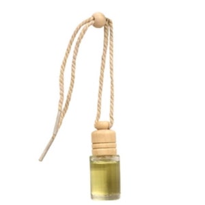 Puede incluir: Una pequeña botella de vidrio con una tapa de madera y una cuerda para colgar. La botella está llena de un líquido transparente y está diseñada para ser utilizada como ambientador de coche.