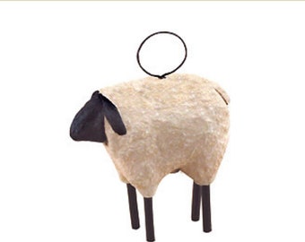 May include: A decorative sheep figurine with a cream-colored body, black head, and dark brown legs. A black wire loop is attached to the top. The sheep is a rustic, farmhouse-style decoration.