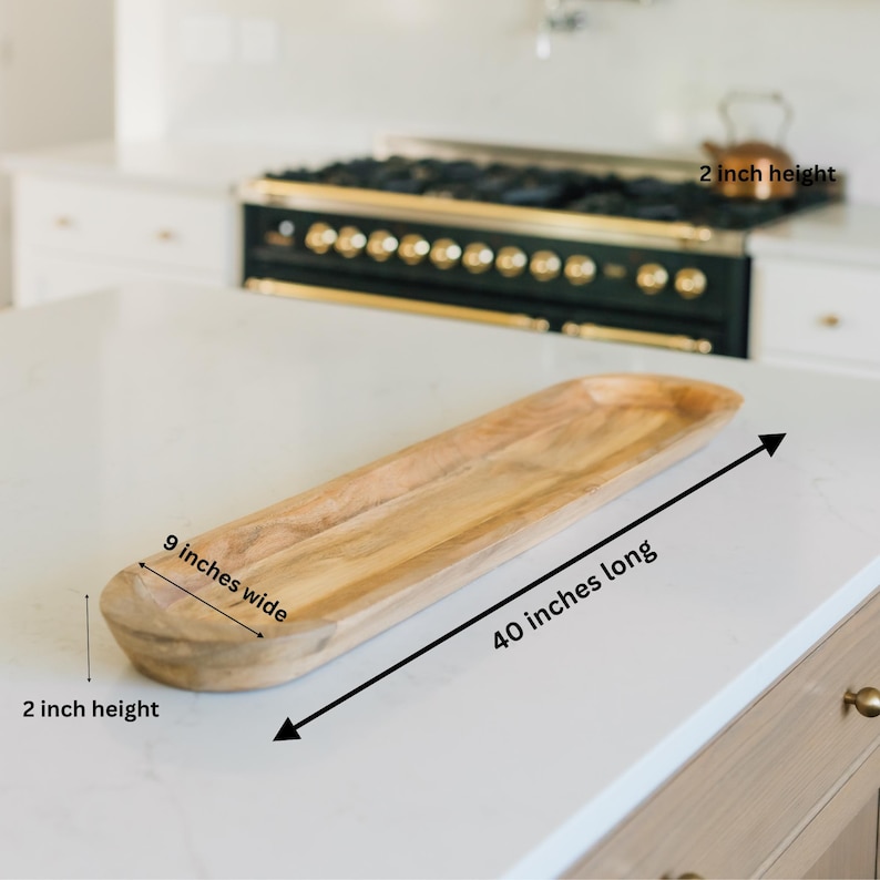 May include: A light-colored wooden serving tray, 40 inches long, 9 inches wide, and 2 inches high. The tray has a natural wood grain and a curved, boat-like shape. It is displayed on a white countertop.