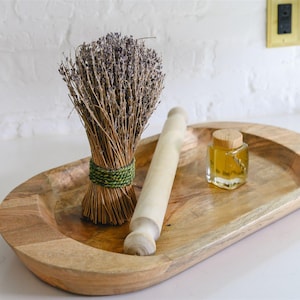 May include: A wooden oval tray holds a bundle of dried lavender tied with green twine, a small rolling pin, and a glass jar with a cork stopper. The tray is made of light-colored wood.