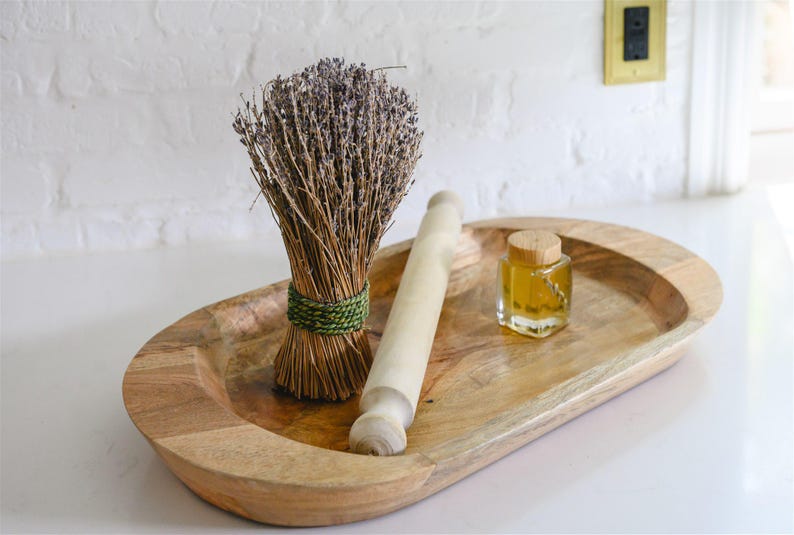May include: A wooden oval tray holds a bundle of dried lavender tied with green twine, a small rolling pin, and a glass jar with a cork stopper. The tray is made of light-colored wood.