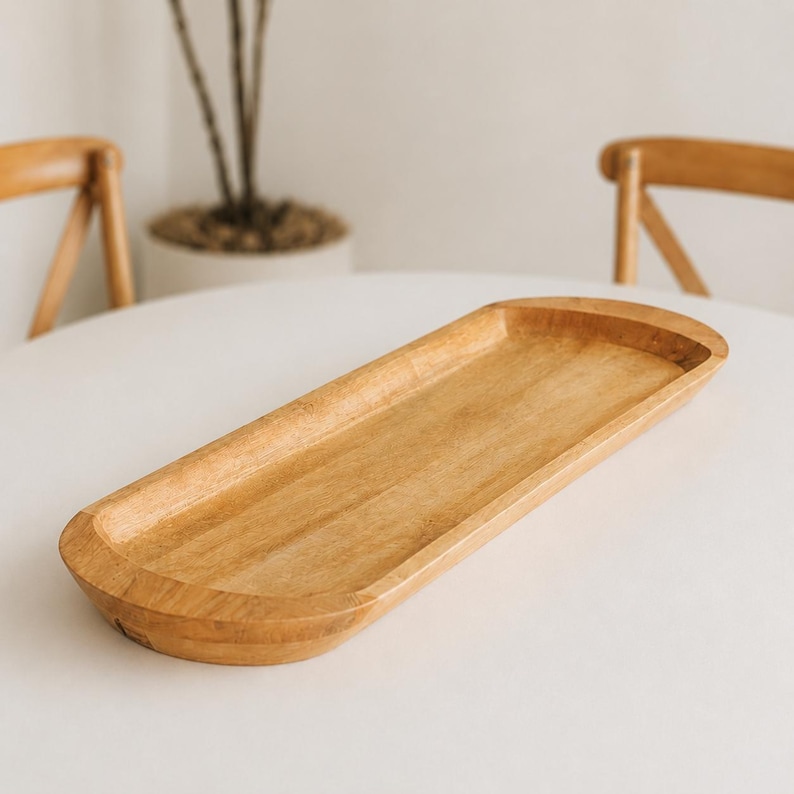 May include: A light brown, wooden serving tray with a rectangular shape and rounded edges. The tray is made of natural wood and has a smooth, polished finish. The tray is empty and sits on a white surface.