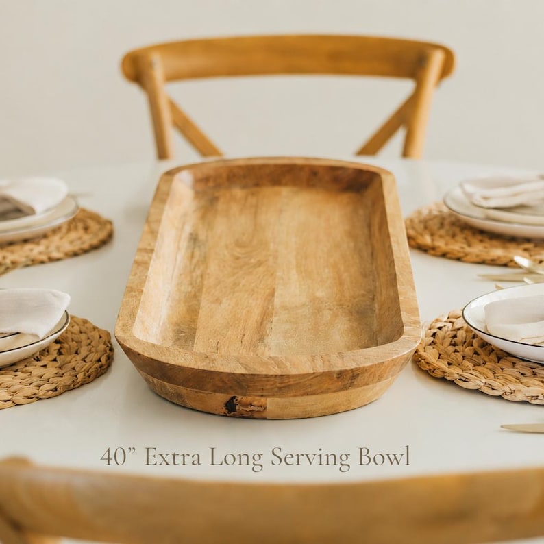 May include: A 40-inch extra long serving bowl made of light-colored wood. The rectangular bowl is on a white table, with place settings and a wooden chair in the background. The bowl is ideal for serving food.