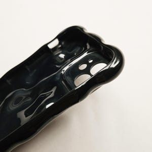 May include: Black phone case with a unique, abstract, liquid-like design. The case has a cutout for the camera lens.