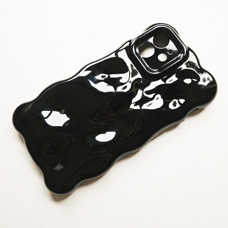 May include: Black phone case with a unique, abstract, liquid-like design. The case has a glossy finish and a raised camera bump.