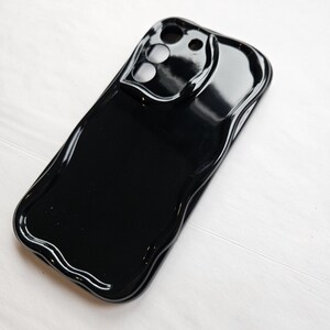 Puede incluir: Carcasa de teléfono negra con un diseño único y derretido. La carcasa tiene una protuberancia de cámara elevada con tres recortes para las lentes.