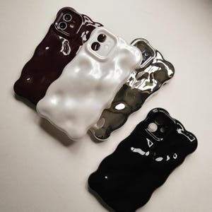 May include: Four phone cases in different colors and textures. The cases are made of a soft, flexible material and have a unique, abstract design. The cases are available in black, white, silver, and burgundy.