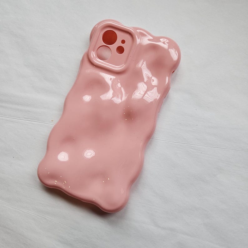 May include: A pink phone case with a textured, melted look. The case has a cutout for the camera lens.