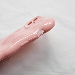 May include: A pink silicone phone case with a raised design. The case has cutouts for the camera and charging port.