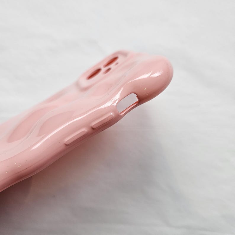 May include: A pink silicone phone case with a raised design. The case has cutouts for the camera and charging port.