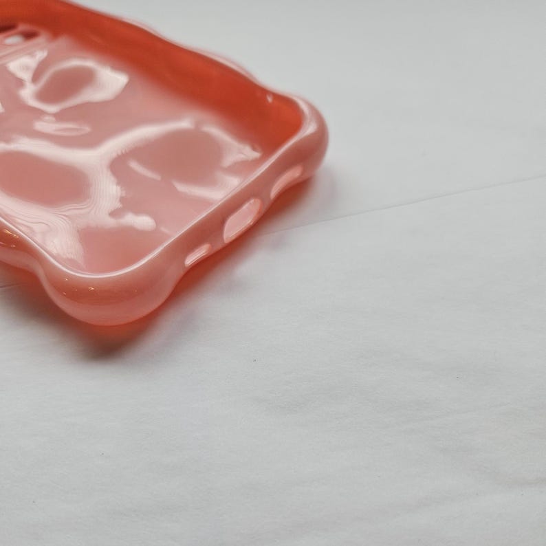 May include: A pink silicone phone case with a smooth, glossy finish. The case has cutouts for the phone's camera and buttons.