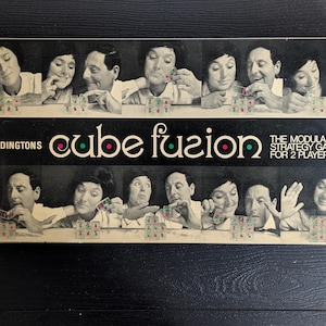 Peut inclure: Boîte de jeu de société vintage "cube fusion" de Waddingtons. L'image en noir et blanc montre des personnes jouant au jeu. Le texte "THE MODULAR STRATEGY GAME FOR 2 PLAYERS" est également visible.